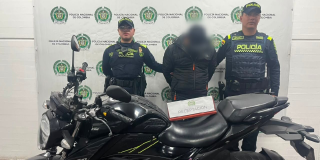 Foto de uniformados de la Policía con el hombre capturado y la motocicleta incautada.
