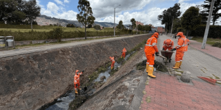 Foto que muestra personas con el uniforme de Aguas Bogotá limpiando un canal de agua