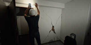 Foto que muestra una persona con un casco revisando una pared con una grieta 