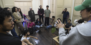 Imagen de varios jóvenes en una aula escuchando a un hombre mayor que habla.