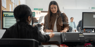 Foto que muesta dos mujeren hablando, computadores y una impresora