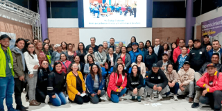Grupo de personas participante en el Cuarto Diálogo Ciudadano del IDIGER en Ciudad Bolívar posan en un auditorio con una pantalla para proyectar presentaciones de fondo.