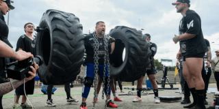 Persona participa en una prueba de fuerza al aire libre mientras levanta dos llantas de gran tamaño sujetas a una estructura metálica con cadenas.
