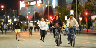 Personas en bicicleta, corriendo y caminando durante una jornada nocturna de actividad física en una vía de Bogotá.