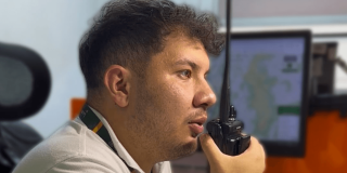 persona utilizando un radio portátil en centro de monitoreo de emergencias, con pantallas de información al fondo para el seguimiento de eventos en Bogotá.