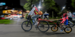 Persona adulta y menor de edad recorren una vía en bicicleta durante una jornada nocturna en Bogotá.