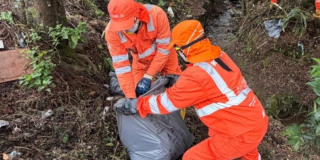 Foto que muestra dos personas levantando una bolsa con residuos 
