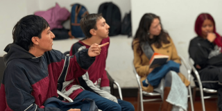 Foto que muestra dos hombres y dos mujeres sentados en escritorios dentro de un salón