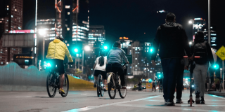 Personas en bicicleta y caminando durante la Ciclovía Nocturna en una vía de Bogotá iluminada por luces urbanas.
