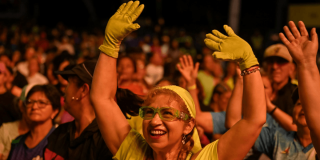 Persona con guantes y gafas de color verde levanta los brazos entre el público durante un evento nocturno al aire libre en Bogotá.