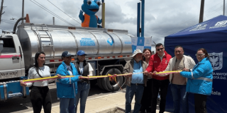 Foto que muestra un grupo de personas sonriendo sosteniendo una cinta y un carrotanque en el fondo
