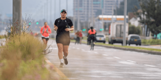 Foto de una persona trotando por una vía de la Ciclovía de Bogotá mientras otras personas realizan actividad física en bicicleta y caminata.