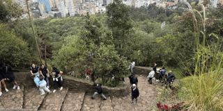 Foto de personas ascienden los escalones del sendero de Monserrate en un día despejado y con vista panorámica de Bogotá.
