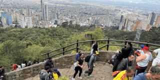 Personas acienden por el sendero de Monserrate con un fondo panorámico de la ciudad de Bogotá donde se observan edificios y zonas residenciales
