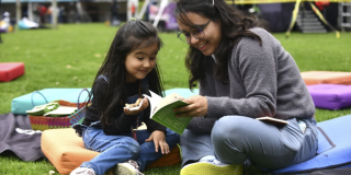 Imagen de una señora con una niña sobre el pasto leyendo un libro de BibloRed