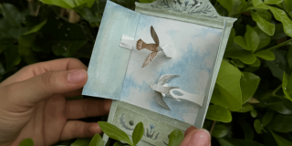 Imagen de una figura de una ave café claro y de otra ave blanca hechas en papel.