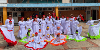 Grupo de personas con trajes folclóricos blancos y detalles de colores durante presentación artística en patio escolar de Bogotá.
