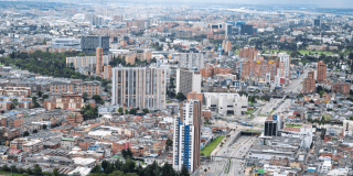 Vista panorámica de Bogotá con edificios residenciales, vías principales, zonas comerciales y amplias áreas urbanas bajo un cielo nublado.