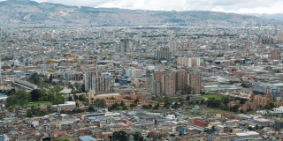 Vista panorámica de Bogotá con edificios, zonas industriales y cerros bajo cielo nublado.