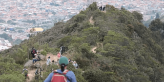 senderos del Parque de Montaña Entrenubes que es recorrido por personas en un día soleado. Al fondo de la imagen se observa una vista panorámica de Bogotá.