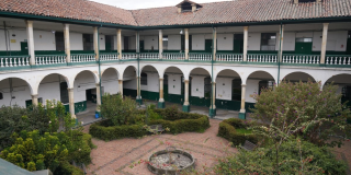 Foto que muestra un edificio de dos pisos con paredes blancas y verdes y un jardín en la mitad 