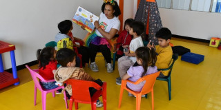 Niños en mesa redonda leyendo un libro con una profesora 