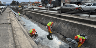 Foto que muestra dos personas con el uniforme de Aguas Bogotá limpiando un canal de agua 