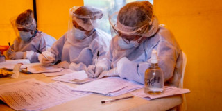 Foto que muestra dos personas con gorro y guantes de enfermería escribiendo en un papel