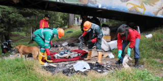 Personal operativo recoge residuos, textiles y otros elementos retirados de una ocupación informal bajo un puente, en una zona verde del humedal Tingua Azul.