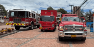 Vehículos del Cuerpo Oficial de Bomberos de Bogotá, entre ellos una máquina extintora, un camión de apoyo y una camioneta de emergencia, estacionados sobre una plazoleta de ladrillo.