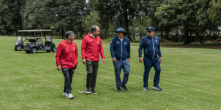 Cuatro personas caminan sobre el césped del campo de golf del Parque La Florida. Dos visten chaquetas rojas y dos chaquetas azules.