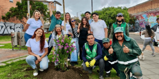 Grupo de personas posa alrededor de un arbusto con flores moradas recién sembrado en una zona verde.