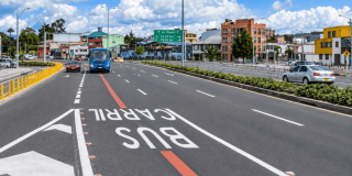 Carril preferencial para buses en la calle 63 de Bogotá, con un bus azul circulando por la vía, señalización vial pintada sobre el pavimento, separadores con vegetación y edificios al fondo.