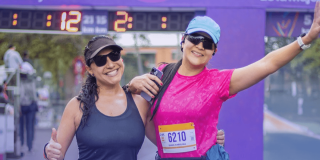 Dos participantes de la Carrera de la Mujer posan frente al arco de meta con números de competencia visibles