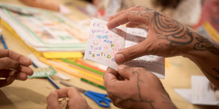 Imagen de manos con tatuajes con libro en hojas pequeño en una biblioteca de Bogotá.