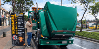 Camión verde de carga estacionado al costado de una vía, con el capó levantado mientras una persona permanece junto al vehículo.