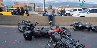 Motocicletas involucradas en un choque permanecen sobre la calzada de una vía principal de Bogotá. En el lugar se observan varias motocicletas caídas, fragmentos dispersos sobre el pavimento y vehículos circulando por los carriles contiguos.