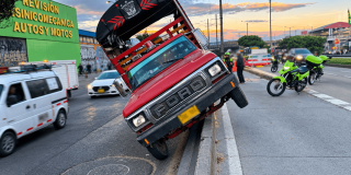 Camión rojo inclinado sobre el separador de una vía de Bogotá, con dos ruedas elevadas. A un costado hay motocicletas de tránsito, personal en la calzada y vehículos circulando en varios carriles.