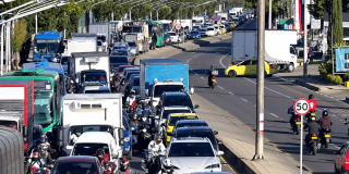 Vista elevada de una avenida urbana con tráfico vehicular intenso y congestionado, donde circulan buses, camiones, automóviles, taxis y motocicletas en Bogotá.