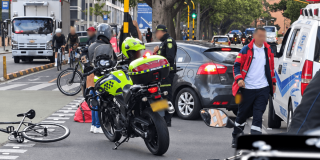 Accidente de tránsito en vía urbana con presencia de motocicleta policial, ambulancia, automóvil particular y bicicleta caída sobre la ciclorruta.