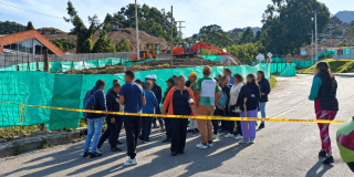 Personas reunidas en una vía observan una situación de movilidad delimitada con cinta amarilla. En el lugar se ven vehículos detenidos, carpas blancas y banderines de colores.