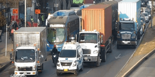 Vehículos particulares, camiones de carga y un bus circulan lentamente en una vía congestionada de Bogotá, con varios carriles ocupados por tráfico denso.