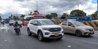 Vehículos particulares, motocicletas y buses circulan por una vía de varios carriles en Bogotá bajo un cielo nublado.