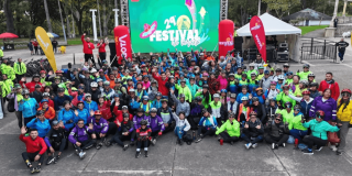 Fotografía grupal de cientos de ciclistas y asistentes al Festival de Verano, reunidos al aire libre frente a un escenario con una pantalla que anuncia la edición 29 del Festival de Verano.