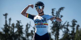 Gabriel Rueda, patinadora bogotana, posa con uniforme de la Liga de Patinaje de Bogotá y casco deportivo en una pista al aire libre, señalando el logo de Bogotá en la camiseta, con árboles desenfocados al fondo y cielo despejado.