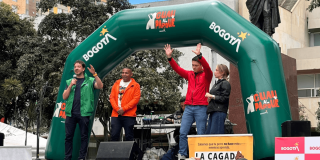 Director del Instituto de Bienestar Animal de Bogotá sobre una tarima bajo un arco inflable verde con logos de Bogotá y “Guau al Parque”, junto a equipos de sonido y un cartel informativo, durante una actividad pública al aire libre en una plaza de Bogotá.