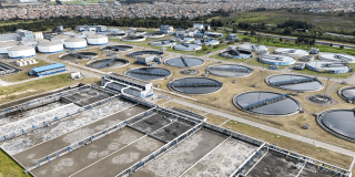 Vista aérea de la PTAR Salitre con múltiples tanques circulares y rectangulares para el tratamiento de aguas residuales, rodeados de estructuras operativas y canales.