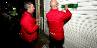 Foto que muestra dos hombres colocando un aviso de sellamiento en un local comercial 