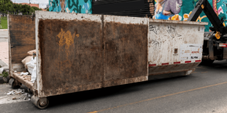 Contenedor metálico de gran tamaño utilizado para la recolección de residuos, ubicado sobre una vía pavimentada.