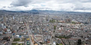 Vista panorámica de Bogotá con edificaciones, vías principales y los cerros orientales al fondo bajo un cielo nublado.